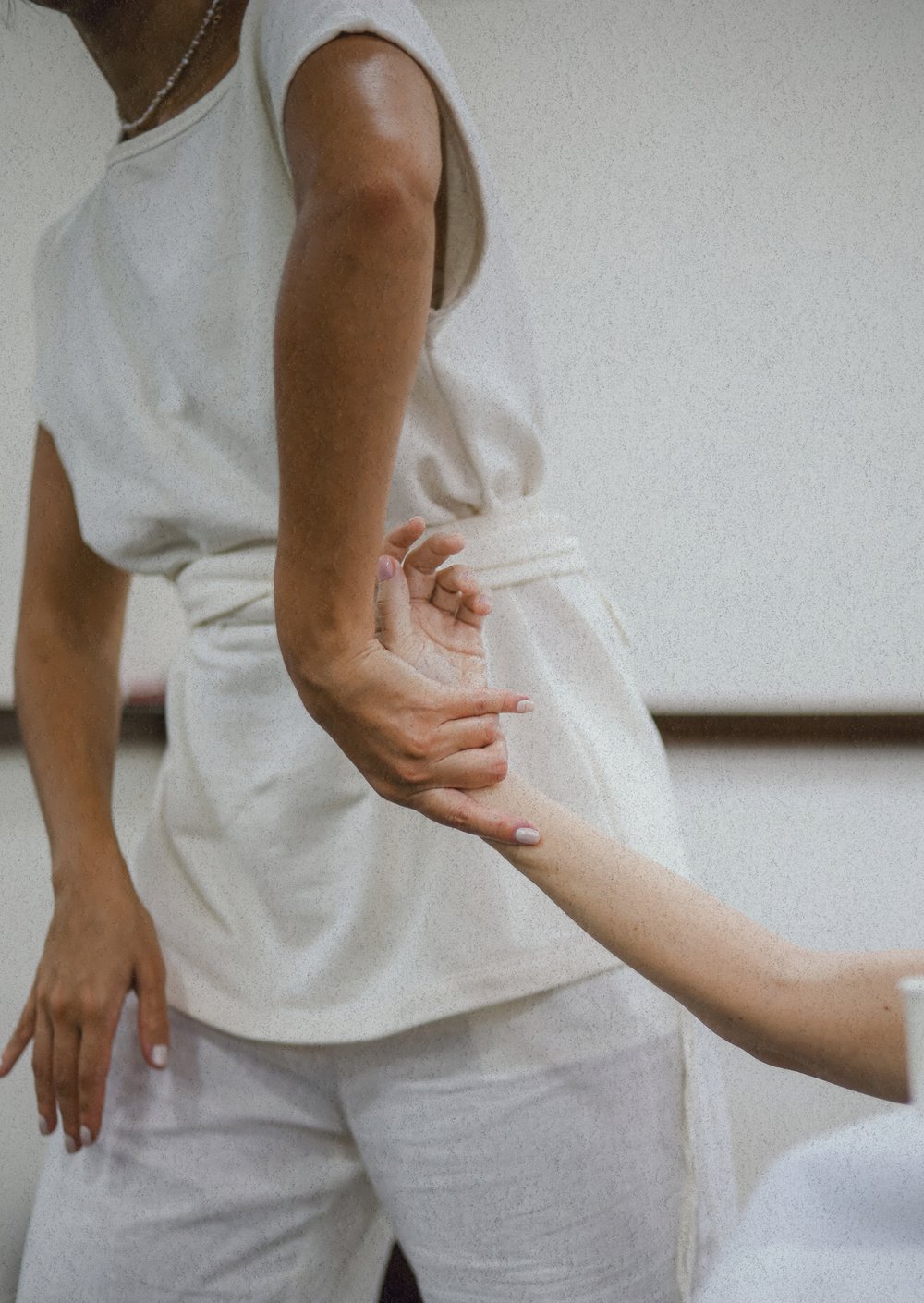 Mãos em gesto de toque sobre um braço, em roupas claras